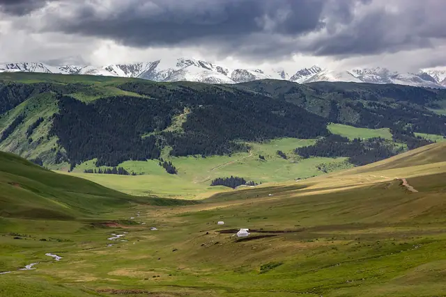 Assy Plateau: wide jailau valley of the Assy plateau with a white yurt and snowy peaks